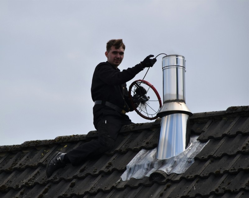 Two certified chimney sweep technicians inspecting a chimney flue with a video camera on a rooftop